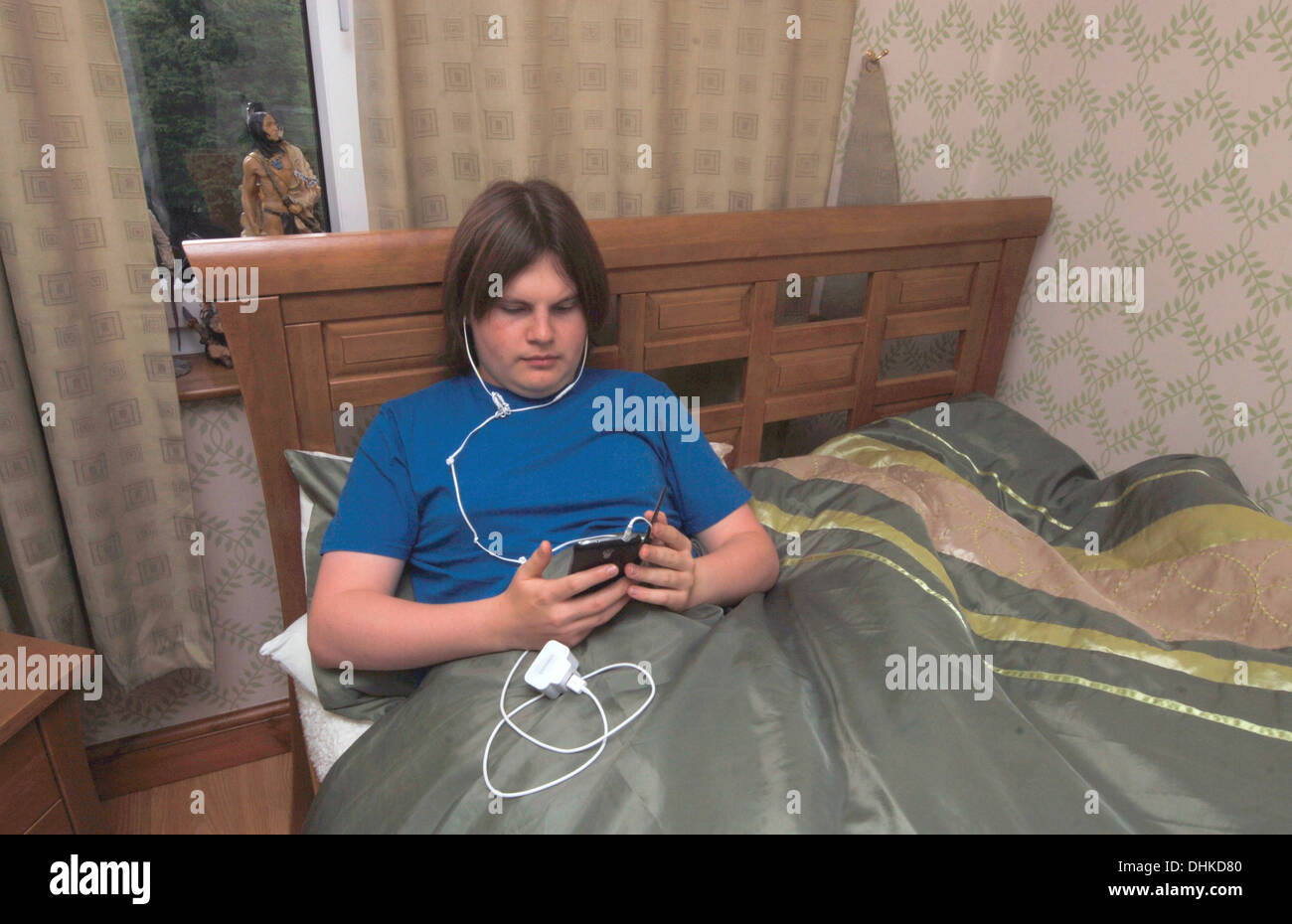 Ein männlicher Jugendlicher in seinem Bett liegt, über sein Mobiltelefon. Stockfoto