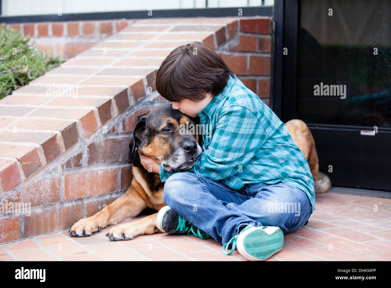 Ein 10 Jahre alter Junge und sein Hund umarmt von einem Backsteingebäude Stockfoto