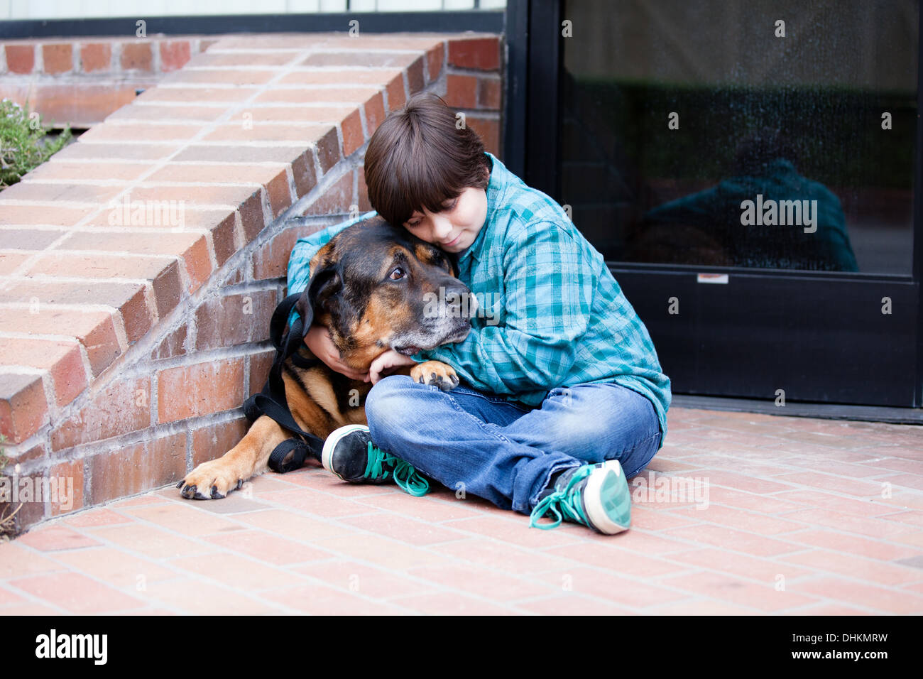 Ein 10 Jahre alter Junge und sein Hund umarmt von einem Backsteingebäude Stockfoto
