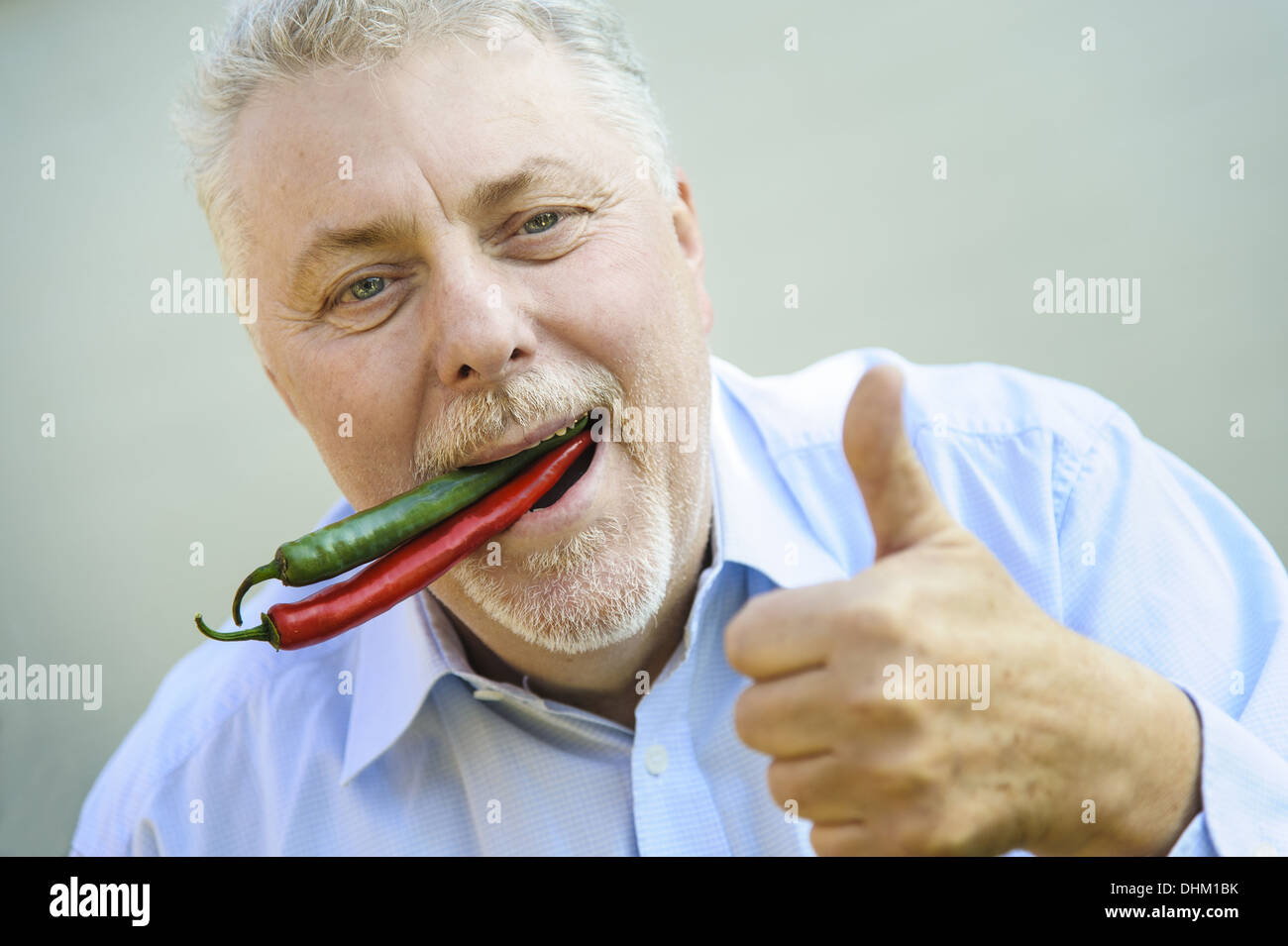 Senior mit roten und grünen Chili in Mund Stockfoto
