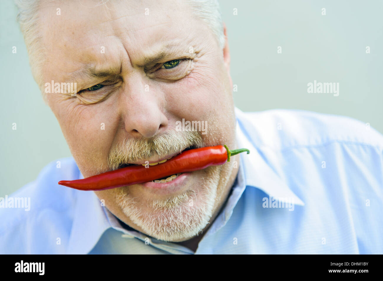 Senior beißt vorsichtig in eine rote chili Stockfoto