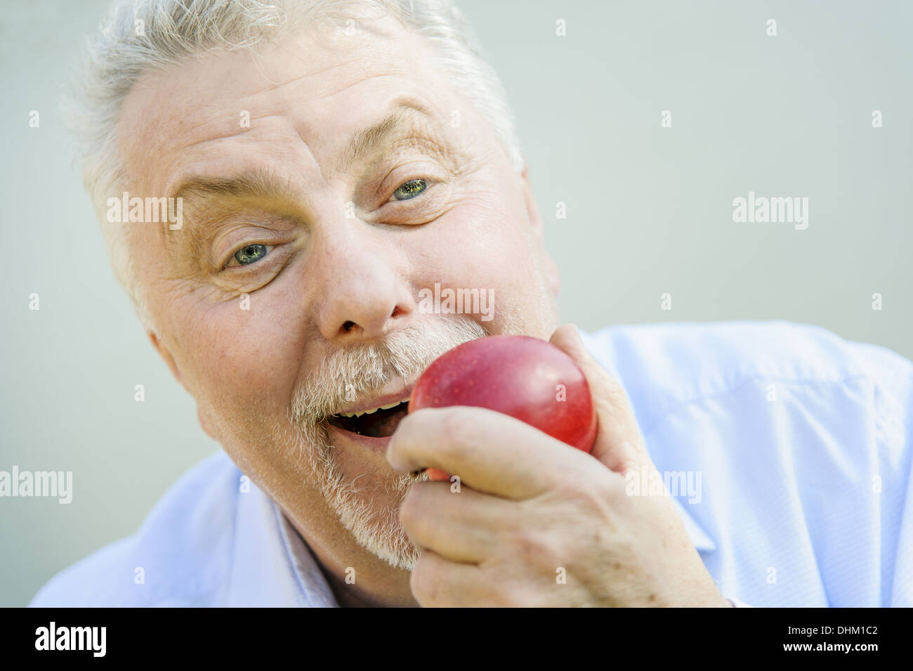 Senior voller Freude isst einen roten Apfel Stockfoto