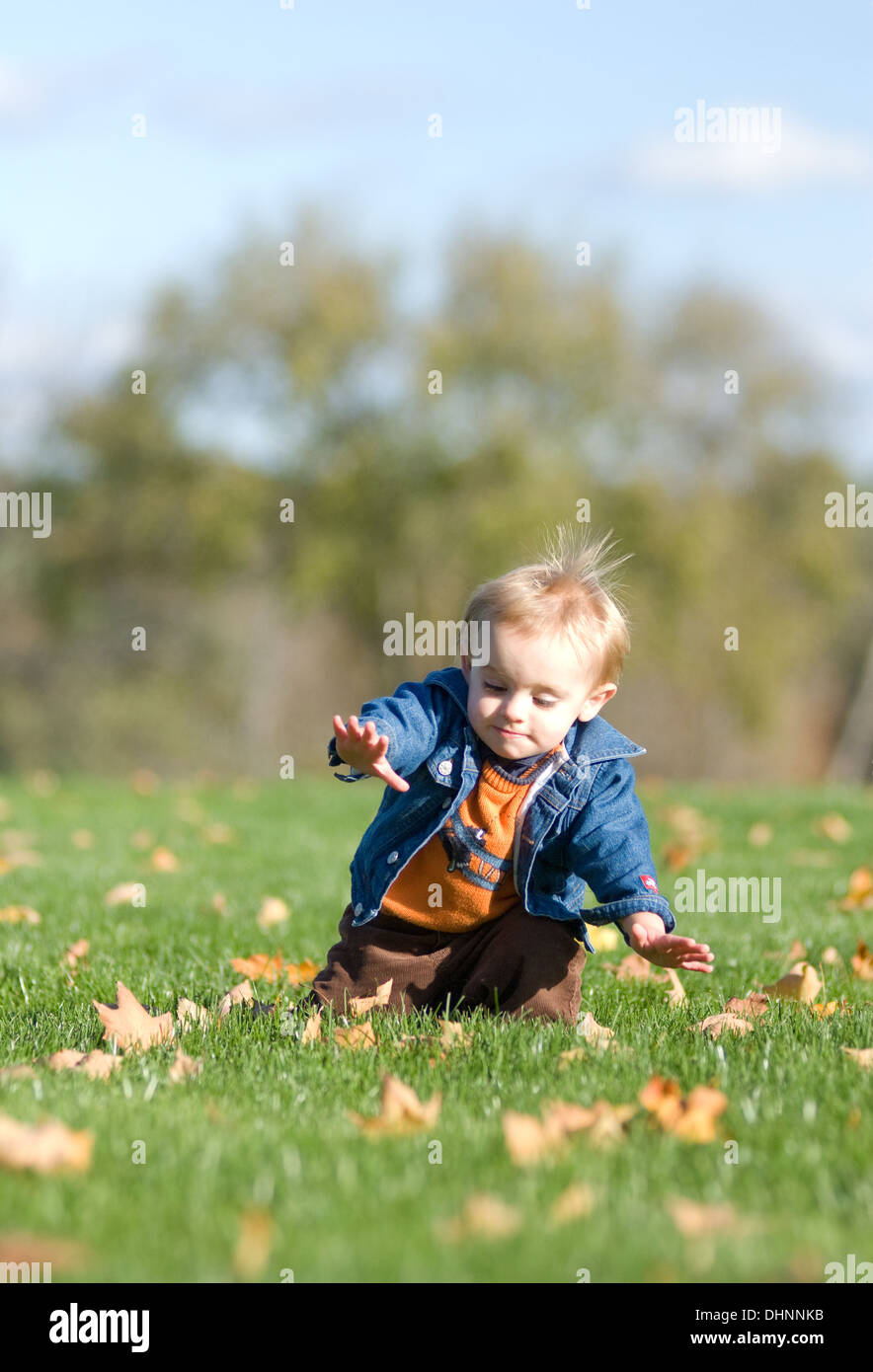 Ein ein-Jahr-alte Blondschopf in einer Jeansjacke Zahnspange selbst für einen Sturz während des Gehens in einem Feld auf ein warmer Herbsttag. Stockfoto