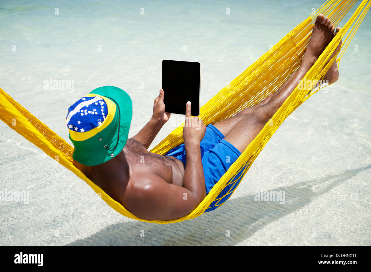 Brasilianischen Mann nutzt Tablet Computer entspannen in der Hängematte am Strand über das Meer Stockfoto