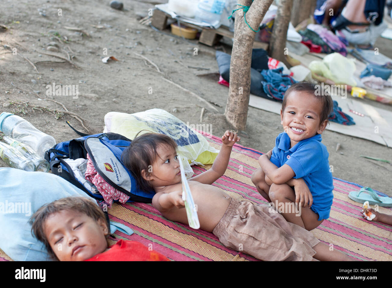Kinder schlafen und spielen auf den Matten an der Seite der Straße in Davao. Stockfoto