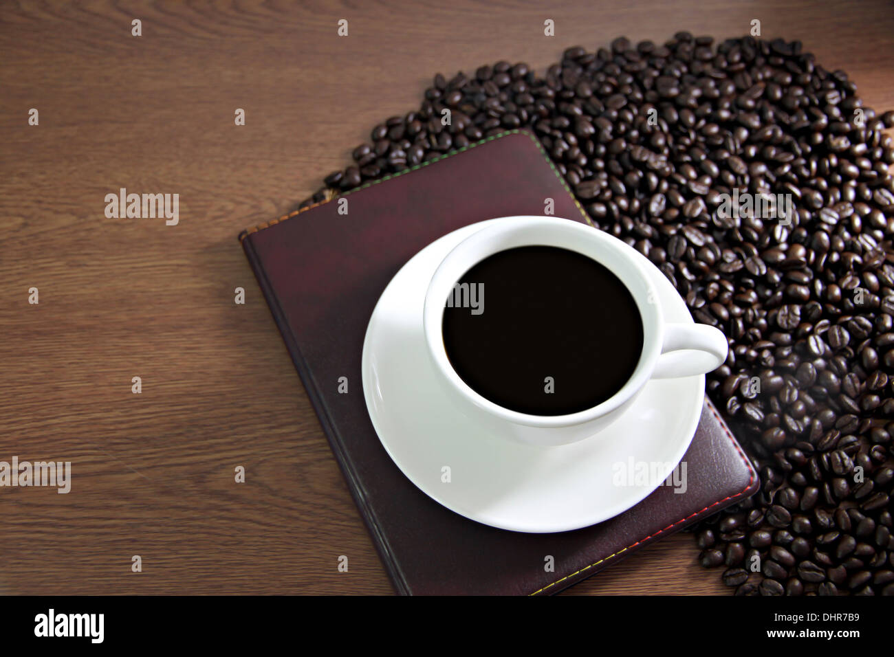 Das Bild Fokus weiße Kaffeetasse und Buch auf dem Tisch altes Holz in der Nähe der Kaffeebohnen. Stockfoto