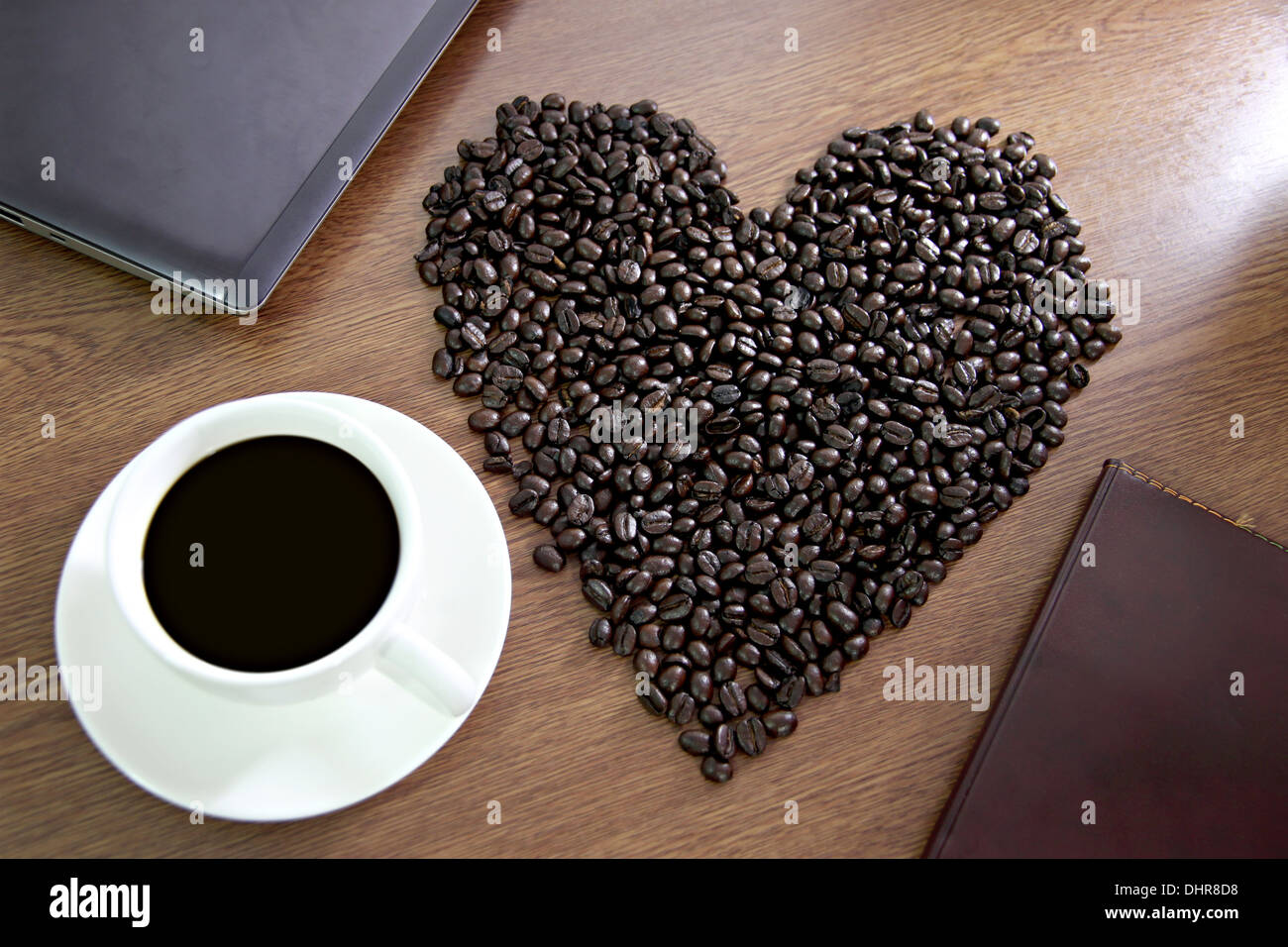 Das Konzept der Blei-Kaffeebohnen angeordnet in einem Herzen in der Nähe von weißen Kaffeetasse geformt. Stockfoto