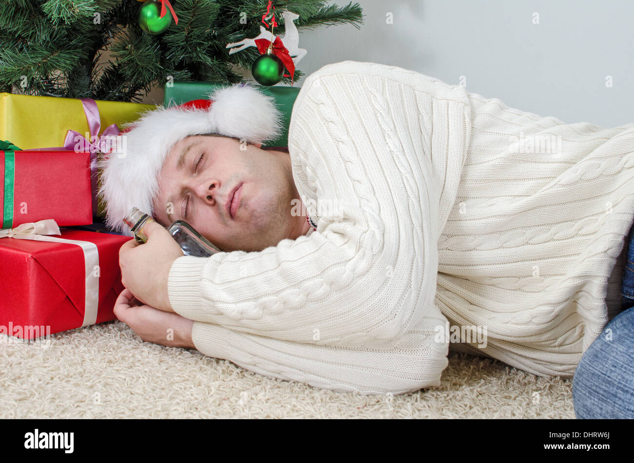 Betrunkener Mann mit Flasche schläft unter Weihnachtsbaum Stockfoto