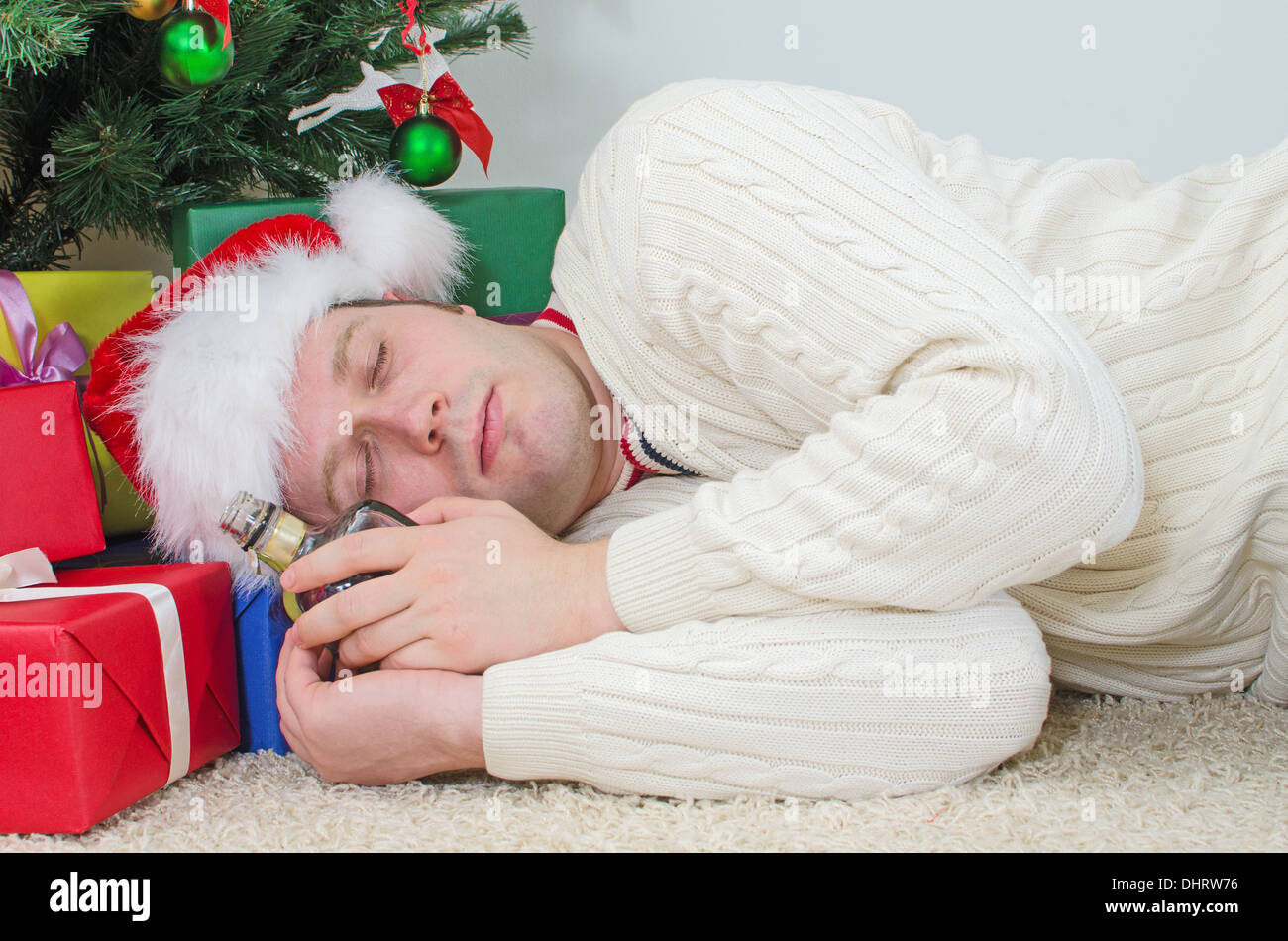 Betrunkener Mann mit Flasche schläft unter Weihnachtsbaum Stockfoto