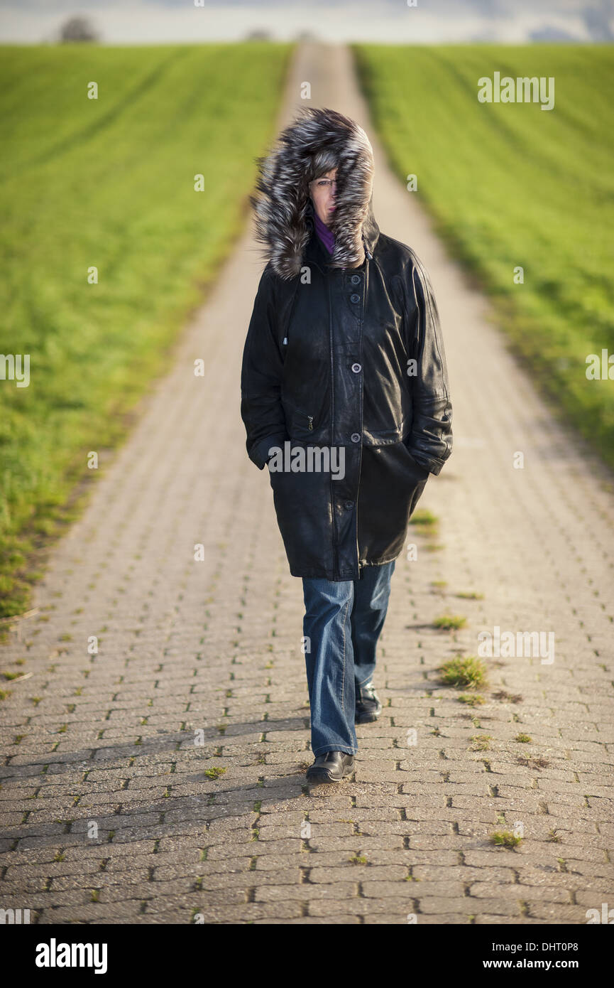 eine Frau geht auf einer Straße zwischen zwei Feldern Stockfoto