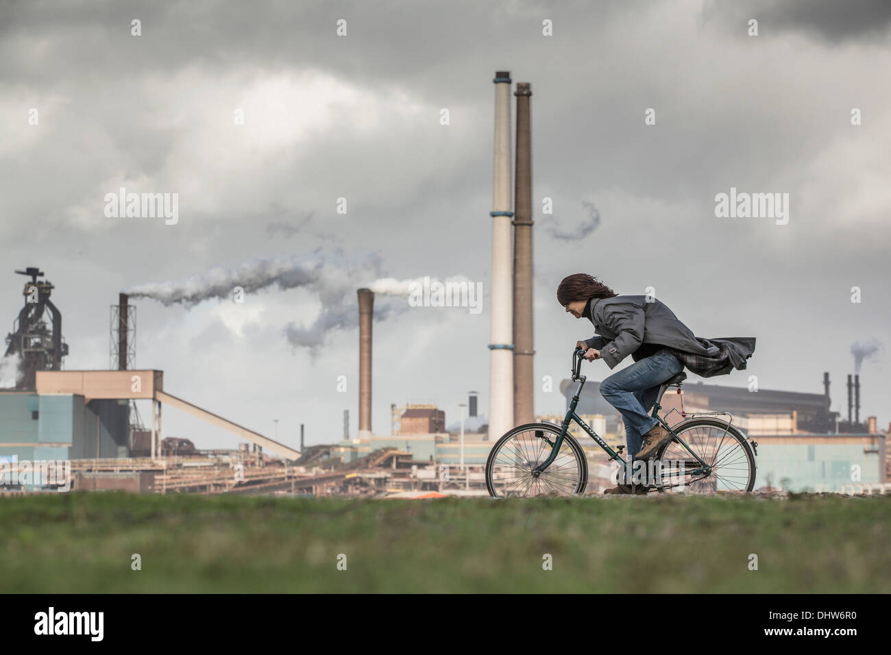 Holland, IJmuiden, Tata Steel Fabrik, Hochöfen. Radfahrer, Frau, versucht zu bleiben aufrecht in StoL Stockfoto