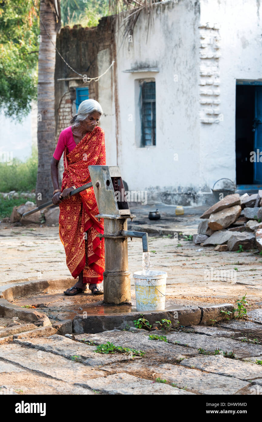 Indische Seniorin Pumpen von Wasser aus einer Hand-Pumpe in einen