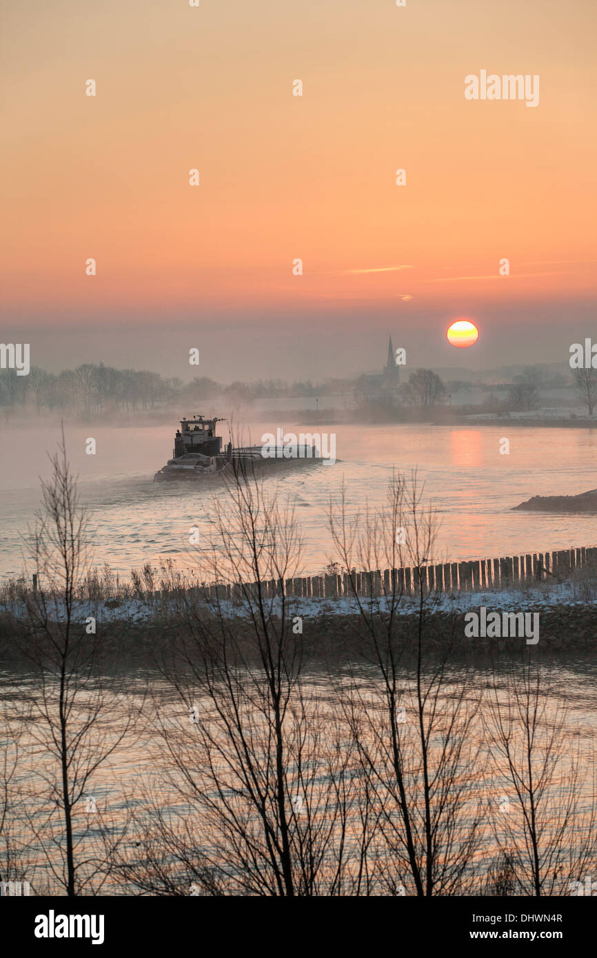 Niederlande, Lopik, Skyline des Dorfes in der Nähe von Lek Fluss. Binnenschifffahrt Frachtboot. Sunrise. Winter Stockfoto