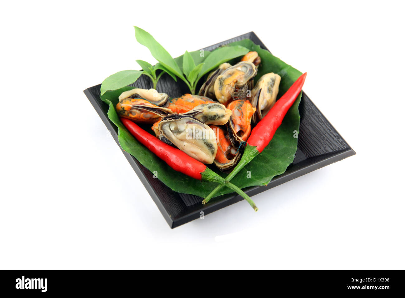 Muscheln und rote Paprika in der schwarzen Schale auf weißem Hintergrund. Stockfoto