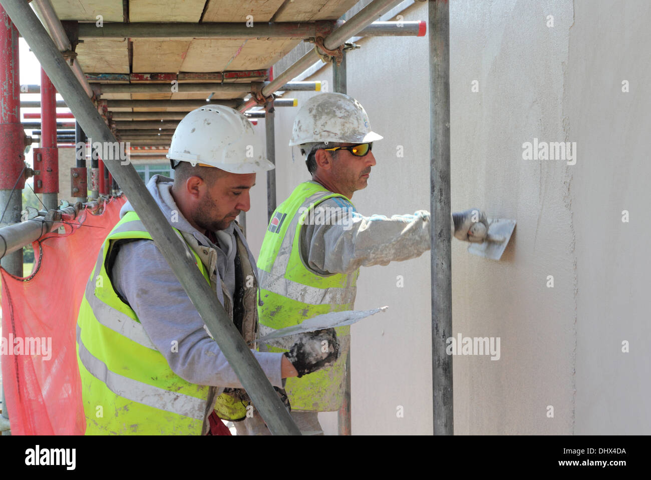 Zwei Arbeiter gelten konkrete Render an der Außenseite des sozialen Wohnungsbaus im Zuge der Sanierungsarbeiten einschließlich der thermischen overcladding Stockfoto