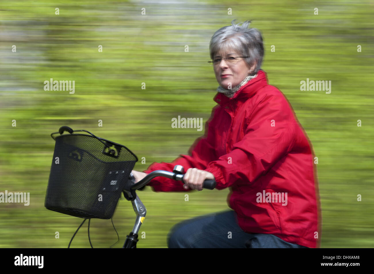 Ältere Frau in einer roten Jacke auf dem Fahrrad Stockfoto