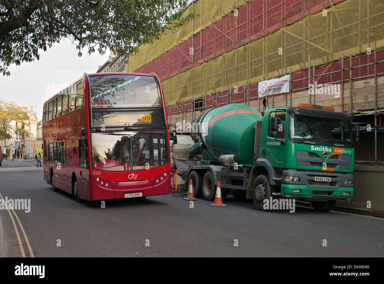 Rot Oxford City Bus überholen einen Betonmischer neben einer großen eingerüsteten Baustelle Stockfoto