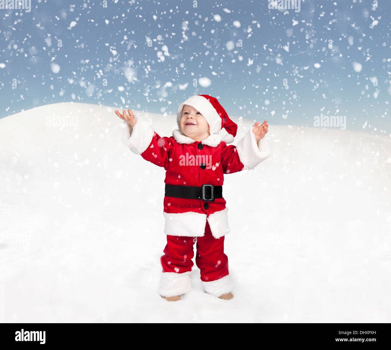 Kleinkind im Weihnachtsmann-Outfit im Schnee stehen und nach oben schauen Stockfoto