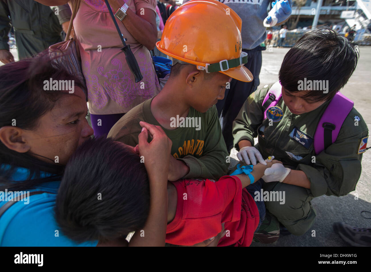 Eine Pilot mit der philippinischen Luftwaffe prüft den intravenösen Port in den Arm eines philippinischen Kindes vor dem Einsteigen in ein PAF C-130 ihr Stockfoto