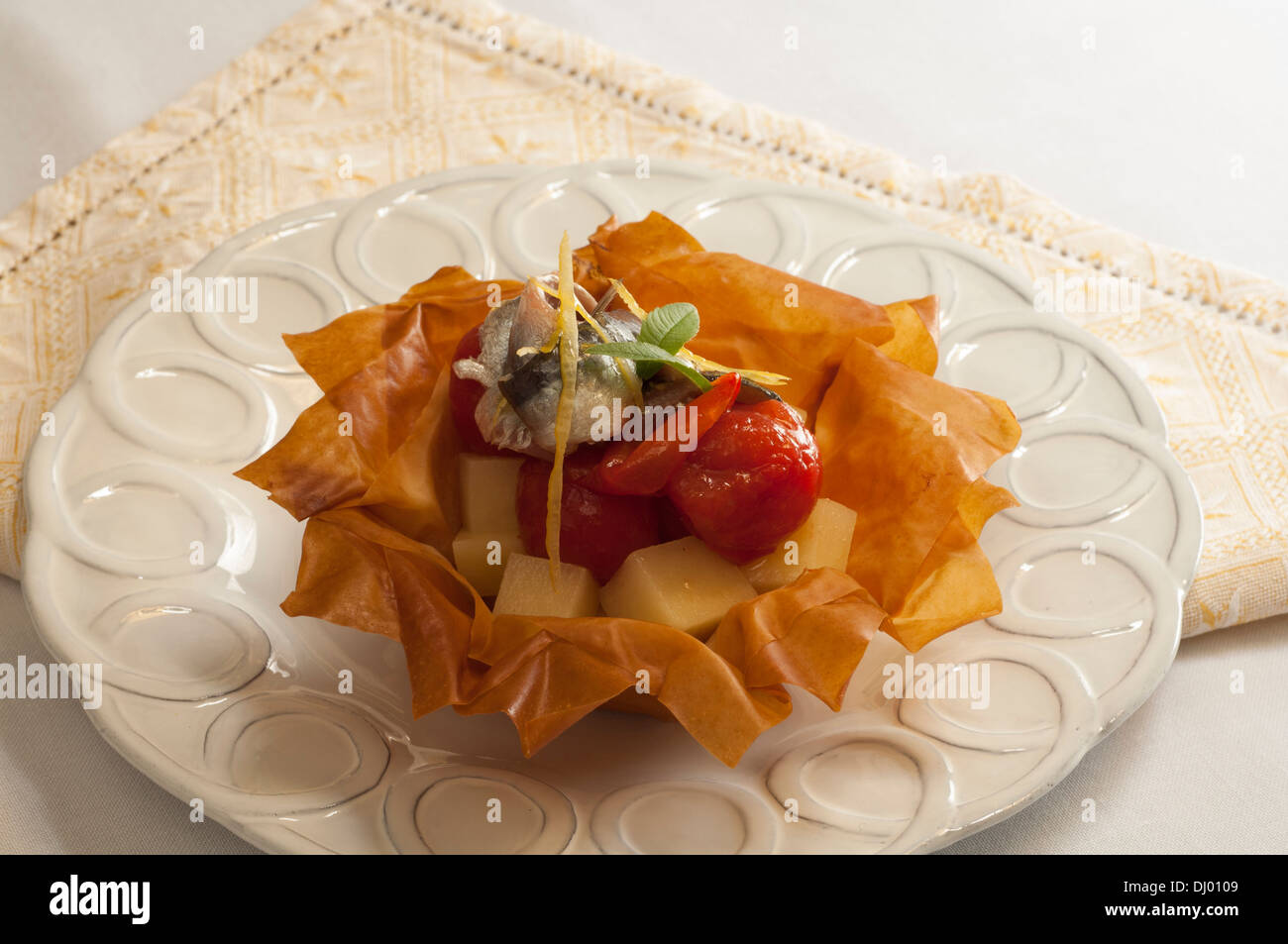 Filo-Teig-Korb mit gebratenen Tomaten, Kartoffeln und marinierte Sardellen mit Majoran Stockfoto