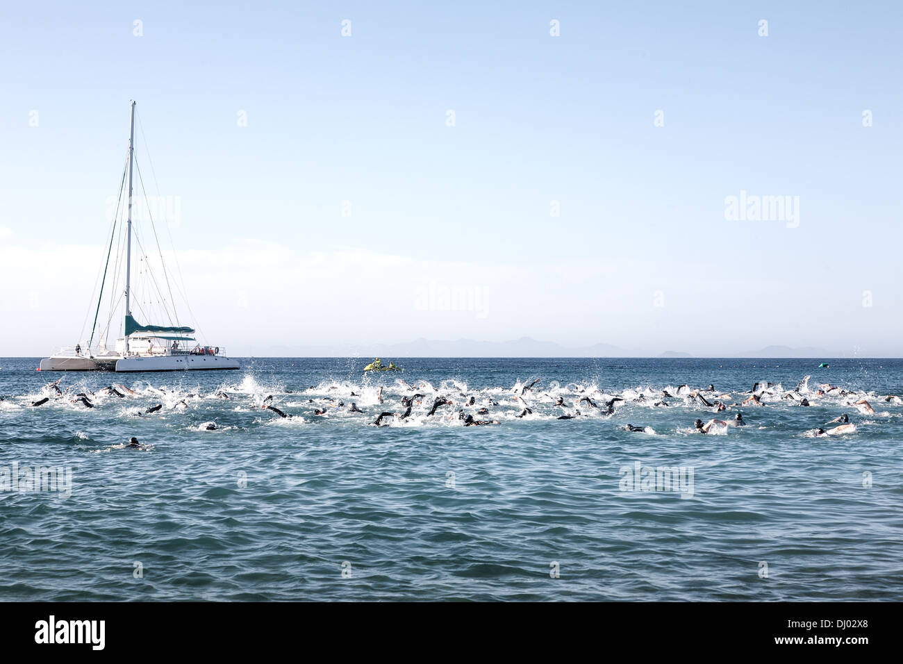 Schwimmer in der Ferne sehen aus wie ein Schwarm Fische mit einer Yacht im Hintergrund Stockfoto