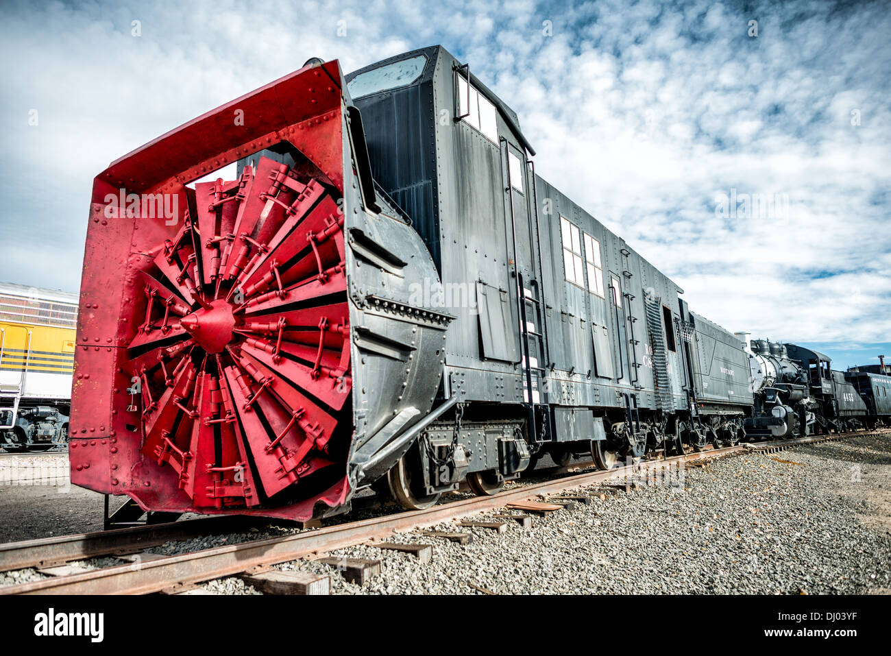GOLDEN, Colorado - Ein Schneepflug im Colorado Railroad Museum in Golden, Colorado. Diese Maschinen verfügten über einen Dampfkessel und Zylinder, um die Rotorblätter nach vorn zu drehen, und einen Zunder an der Rückseite, der die Kohle und das Wasser transportierte, die für den Kessel benötigt wurden. Der Drehpflug war nicht selbstfahrend, sondern erforderte Lokomotiven, um ihn zu schieben. Die großen Klingen an der Vorderseite hackten bei Schnee und die Rutsche wurde zu beiden Seiten von den Ketten weg geleitet. Stockfoto