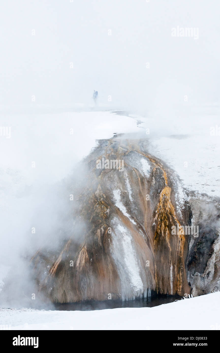Bunten Mineralien absteigend zu einem Pool mit ein einsamer Wanderer in den Dampf an einem Wintermorgen am Yellowstone eingefroren Stockfoto