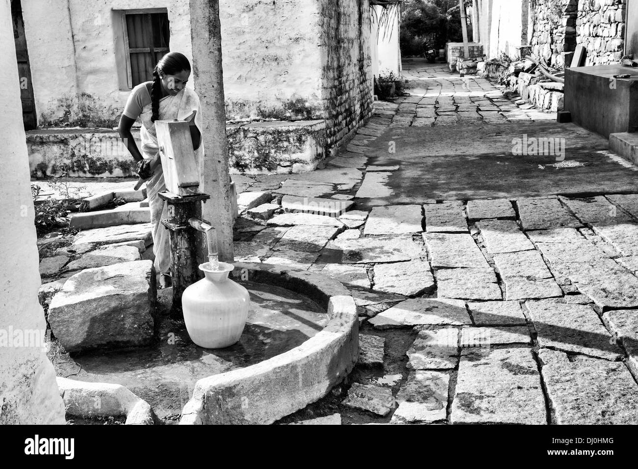 Indische Frau Füllung Kunststoff Wassertopf aus einem ländlichen Dorf Handpumpe. Andhra Pradesh, Indien. Monochrom Stockfoto