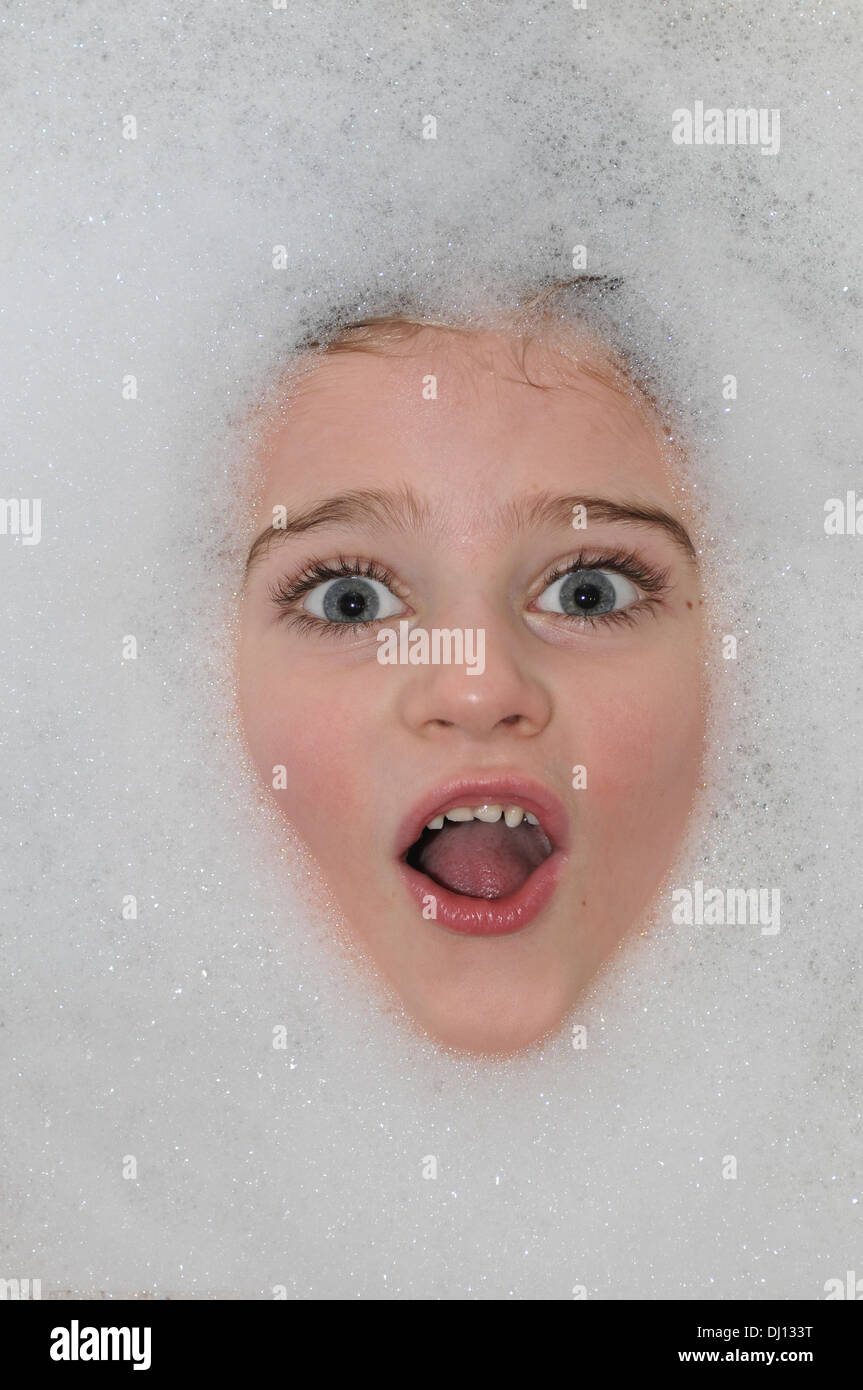 Ein Kind sieht glücklich in der Badewanne, umgeben von Luftblasen Stockfoto