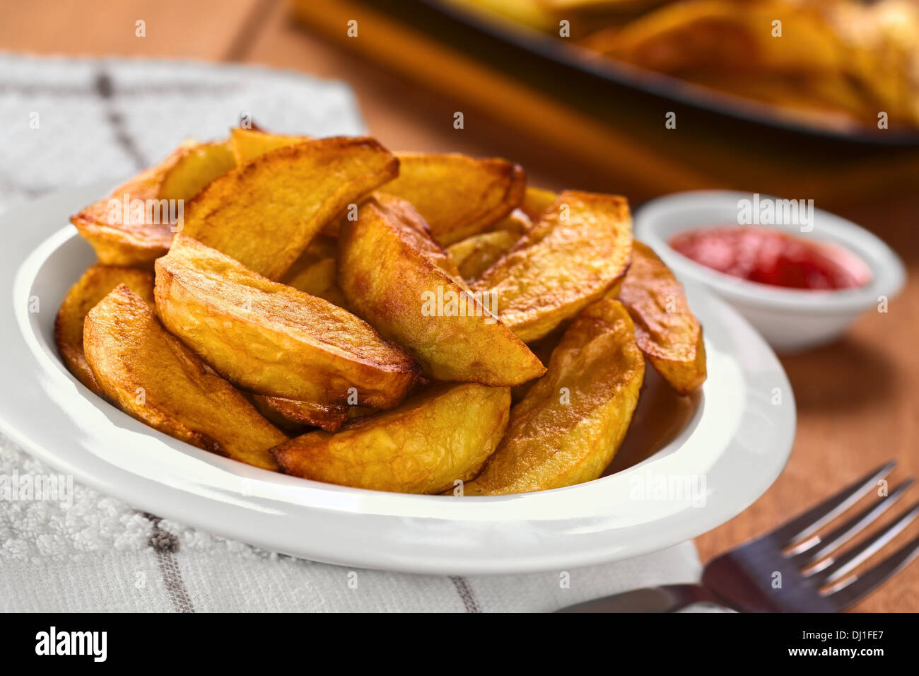 Frische hausgemachte knusprig gebratene Kartoffel Wedges auf Teller mit Gabel auf der Seite und Ketchup in den Rücken Stockfoto