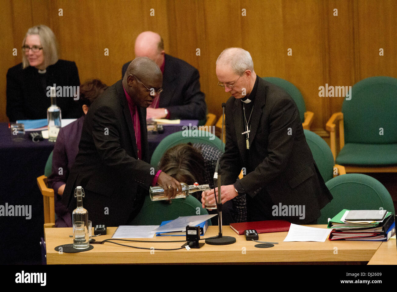 London UK. 19. November 2013. Dr. John Sentamu der Bischof von York gießt einen Schluck Wasser, der Erzbischof von Canterbury Justin Welby bei der jährlichen Generalsynode als die der Church Of England bereitet sich auf die Debatte darüber, ob Frauen Bischöfe erlauben. Stockfoto