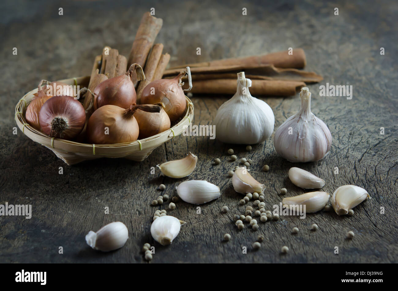 Zwiebel und Zimtstange in Korb, Knoblauch und Pfefferkörner auf Holzbrett (Zutaten) Stockfoto