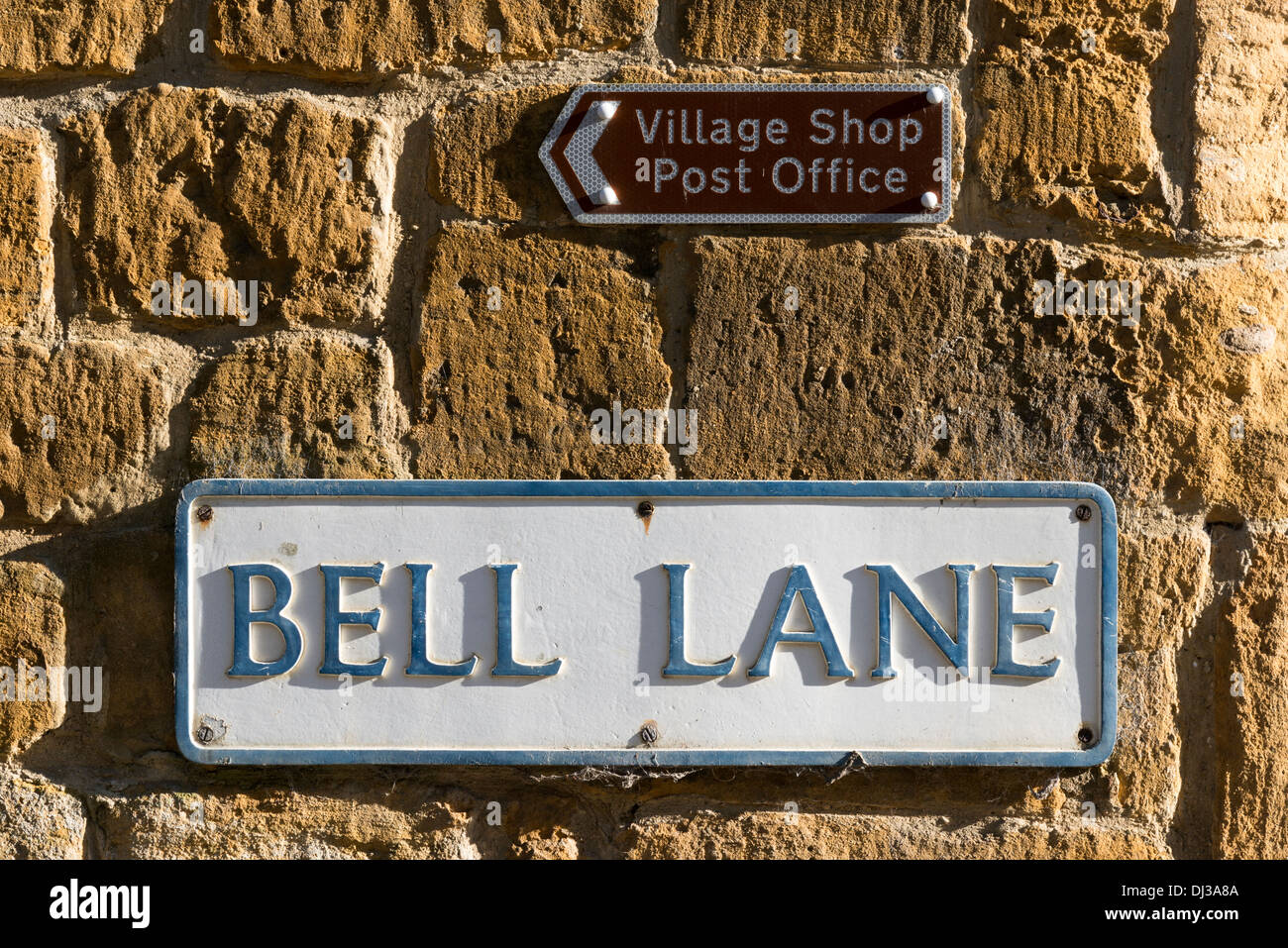 Name Verkehrszeichen und Wegweiser zu den Dorfladen und Post auf einem Cotswold Kalkstein Mauer in Blockley Cotswolds UK Stockfoto