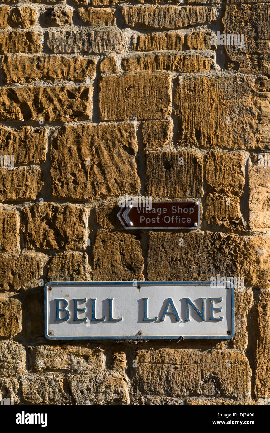 Name Verkehrszeichen und Wegweiser zu den Dorfladen und Post auf einem Cotswold Kalkstein Mauer in Blockley Cotswolds UK Stockfoto