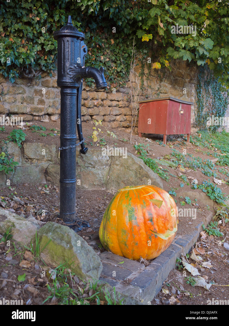 Ein Halloween-Kürbis neben einer Hand betriebenen Wasserpumpe. Stockfoto