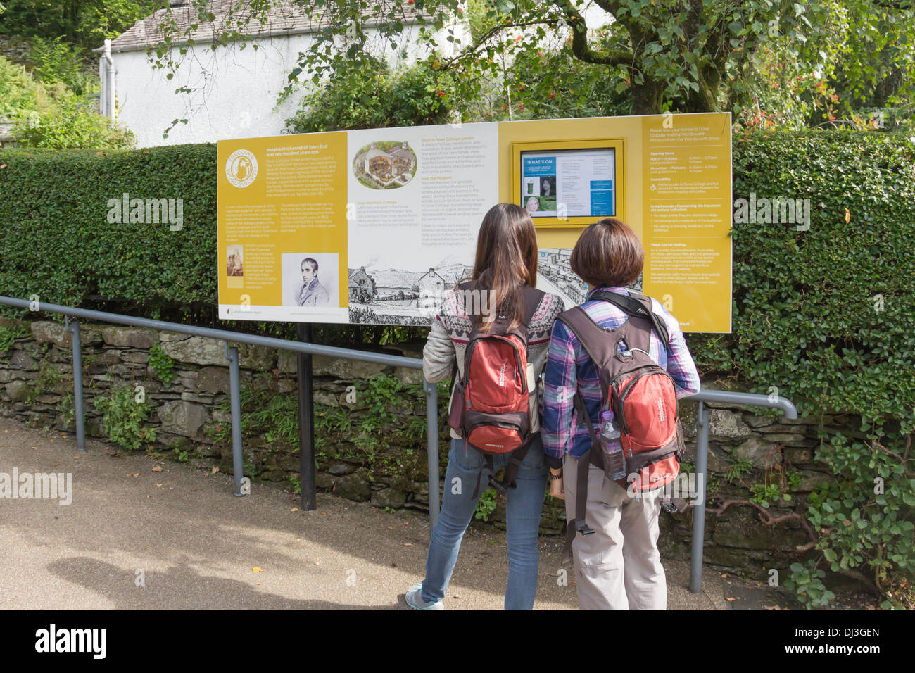 Zwei junge asiatische Frauen lesen die Informationstafel über das William Wordsworth-Museum nahe dem Eingang zur Dove Cottage in Grasmere. Stockfoto