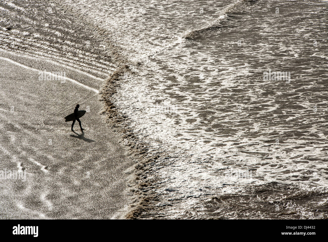Silhouette Surfer im Bild gegen ein fast metallisches Reflexion des Lichtes auf dem Wasser im Saunton Sands Beach, Devon, UK Stockfoto