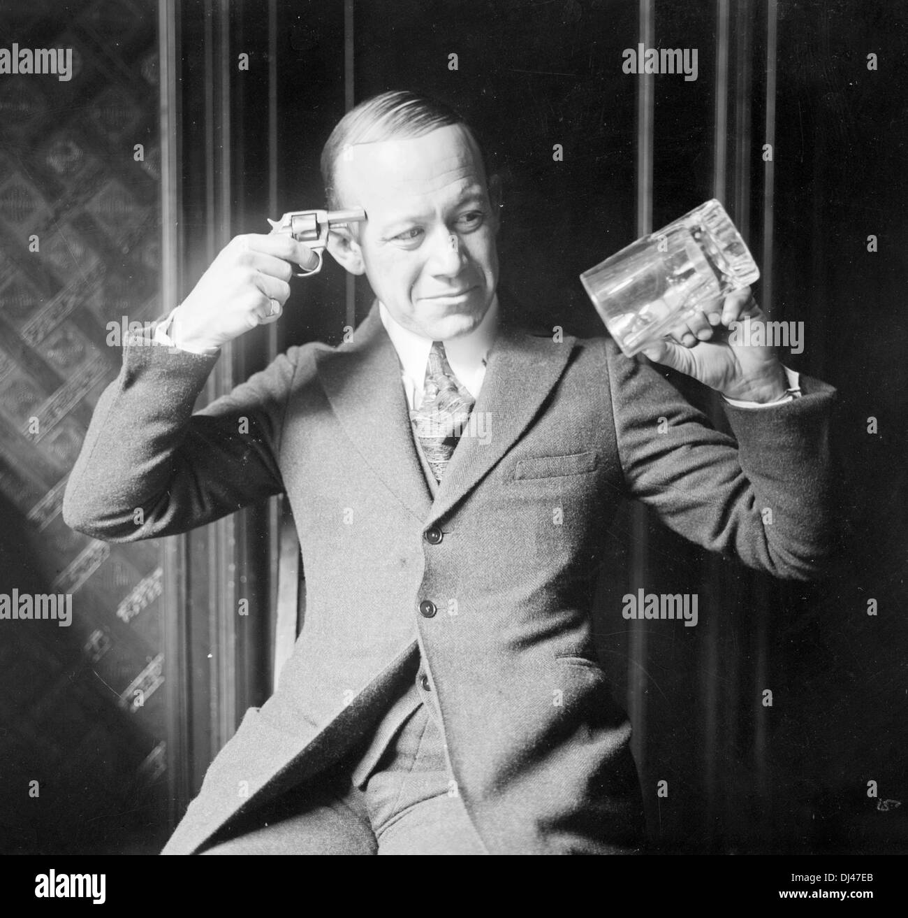 Komiker & Sänger Ernest Hare hält eine leere Bier Becher in einer Hand und hält einen kleinen Revolver an den Kopf mit der anderen. Stockfoto