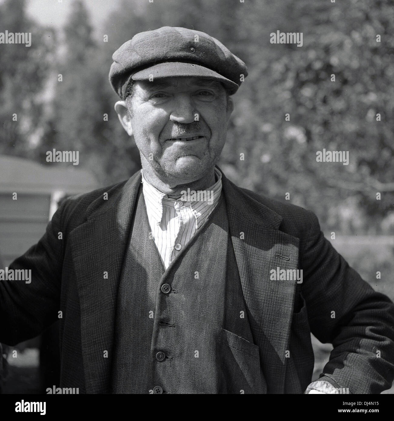 Historisches Bild, 1950s. Porträt eines stolzen kleinen Halters oder Kleinbauern in der Kleidung der Ära und einer flachen Mütze, auf seinem Land stehend, Norfolk, England, Großbritannien. Stockfoto
