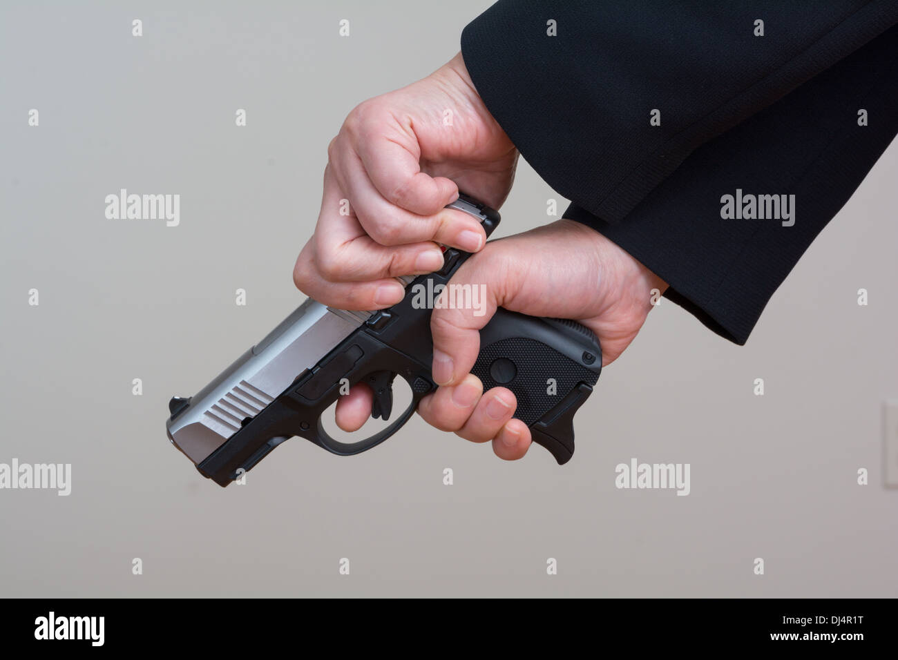 Nahaufnahme von Frau im Business-Anzug Spannen einer Handfeuerwaffe auf grauem Hintergrund Stockfoto