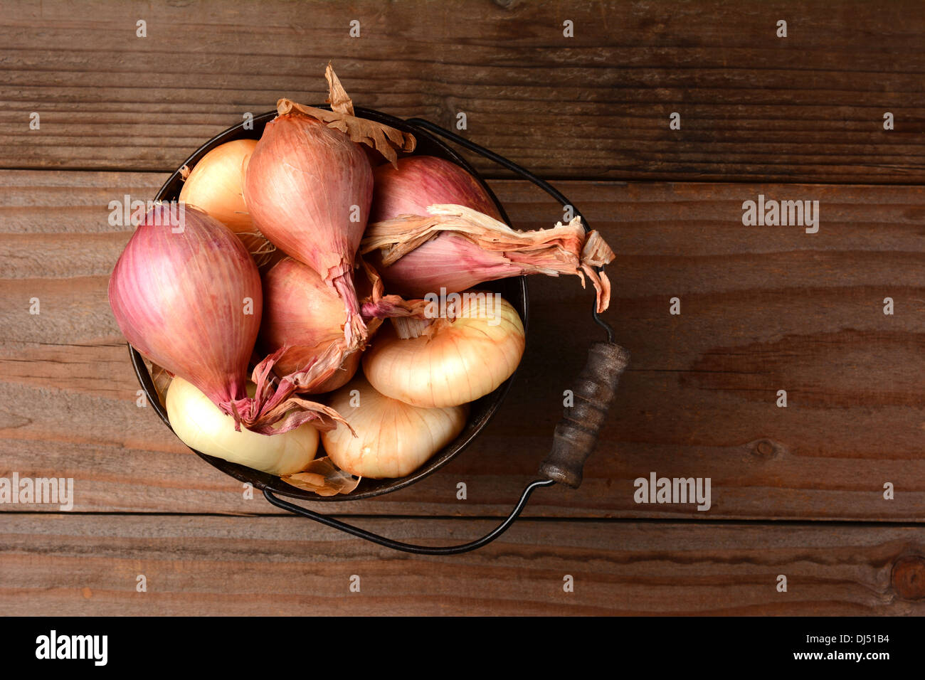 Draufsicht auf Zwiebeln und Schalotten in einen Eimer auf einem rustikalen Holztisch. Querformat. Stockfoto