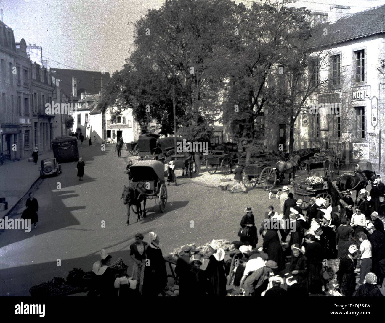 Historisches Bild aus dem Jahr 1930s, das eine Straße in Lüttich, Belgien, zeigt, in der Einheimische an einem Markt für Kleidung unter freiem Himmel teilnehmen. Ein Pferd & Wagen geht die Straße hinunter. Stockfoto