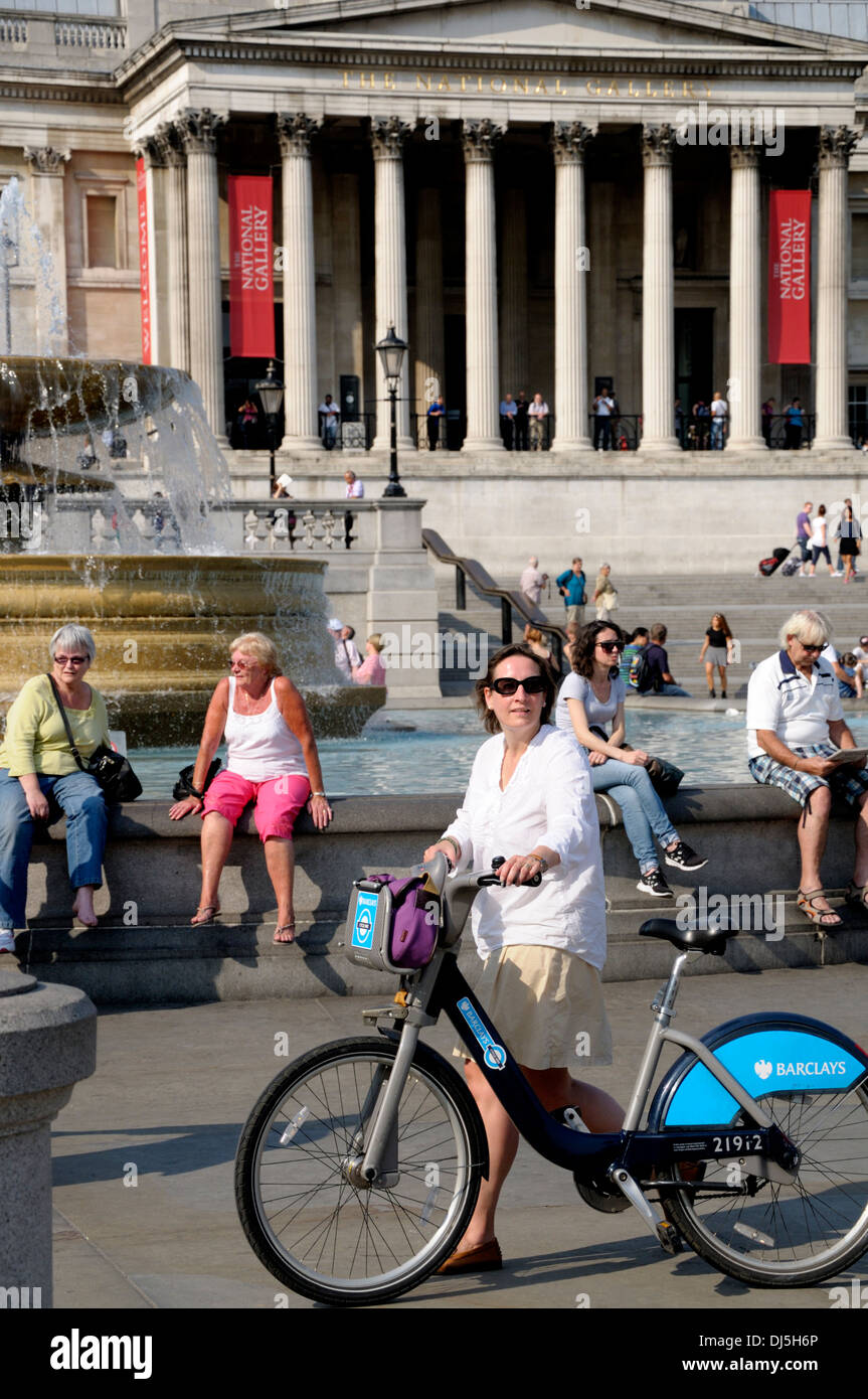 London, England, Vereinigtes Königreich. Trafalgar Square - Frau schob 'Boris Bike' - Zyklus zu mieten Stockfoto