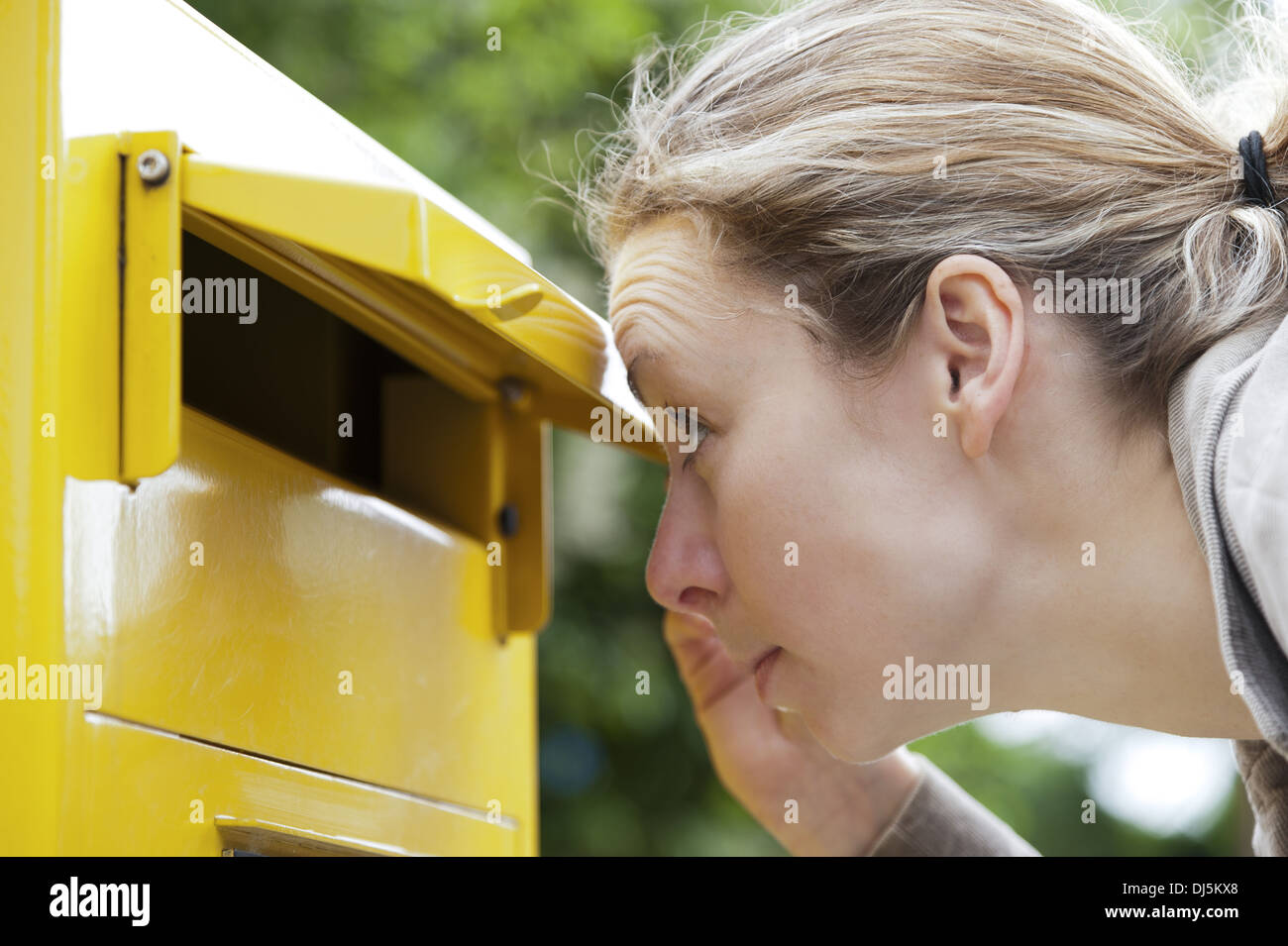junge Frau schaut neugierig in ein Postfach Stockfoto