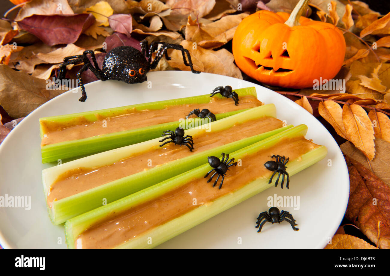 Sellerie-sticks mit Erdnussbutter, Halloween Spinnen und eine lächelnde Jack-o-Laterne auf bunten Herbstlaub Stockfoto