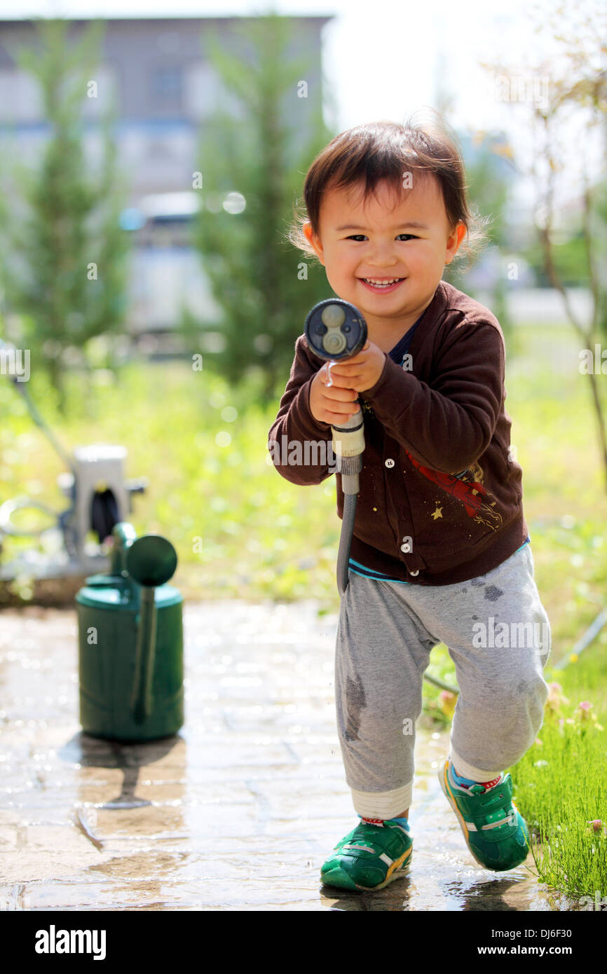 Ein junges Kind junge Lächeln auf den Lippen und das Spiel mit einem Wasserschlauch. Er soll den Betrachter zu sprühen. Stockfoto