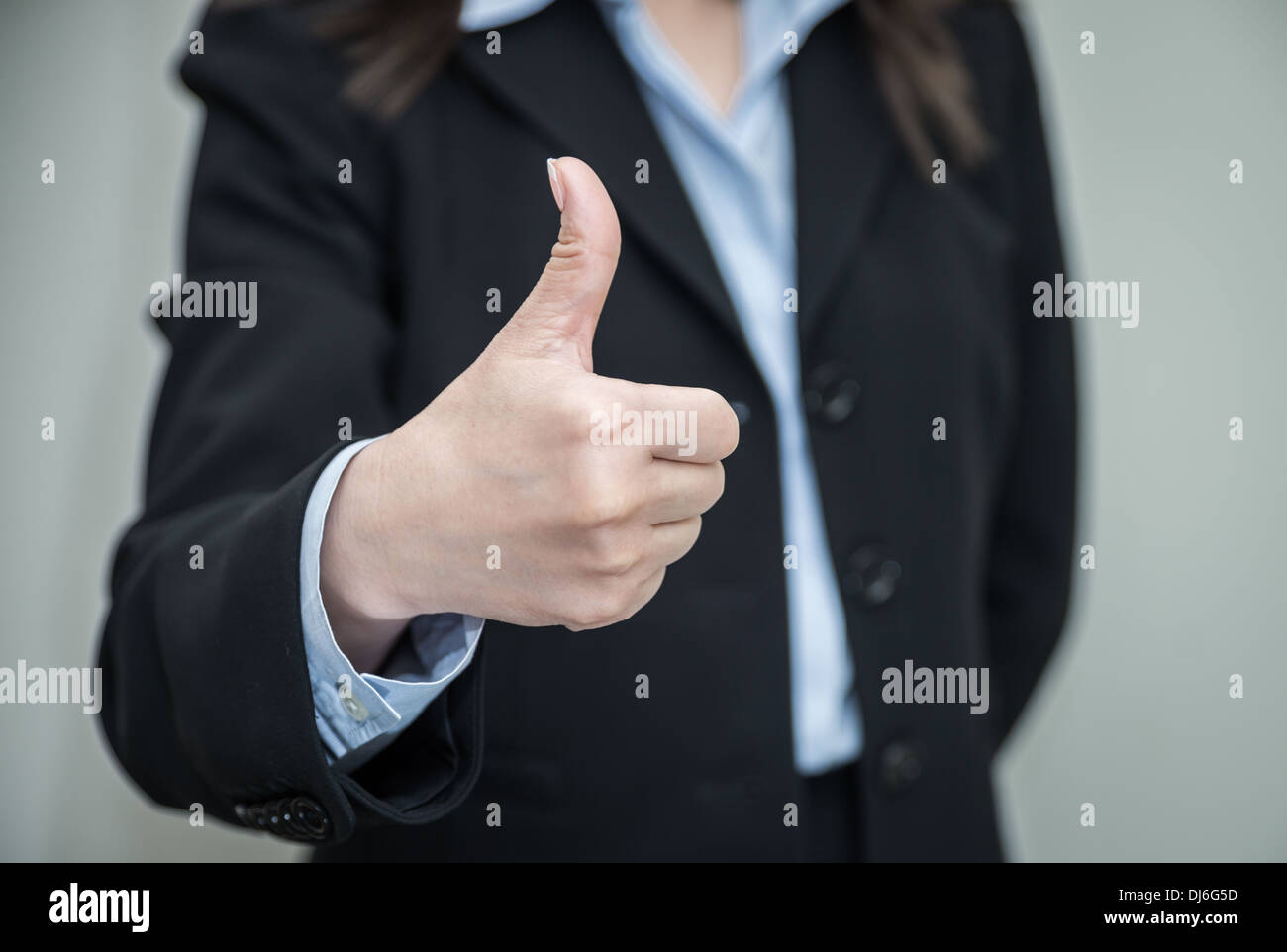 Berufstätige Frau in der Wirtschaft gebende Daumen Schlüpf in Zustimmung auf grauem Hintergrund Stockfoto