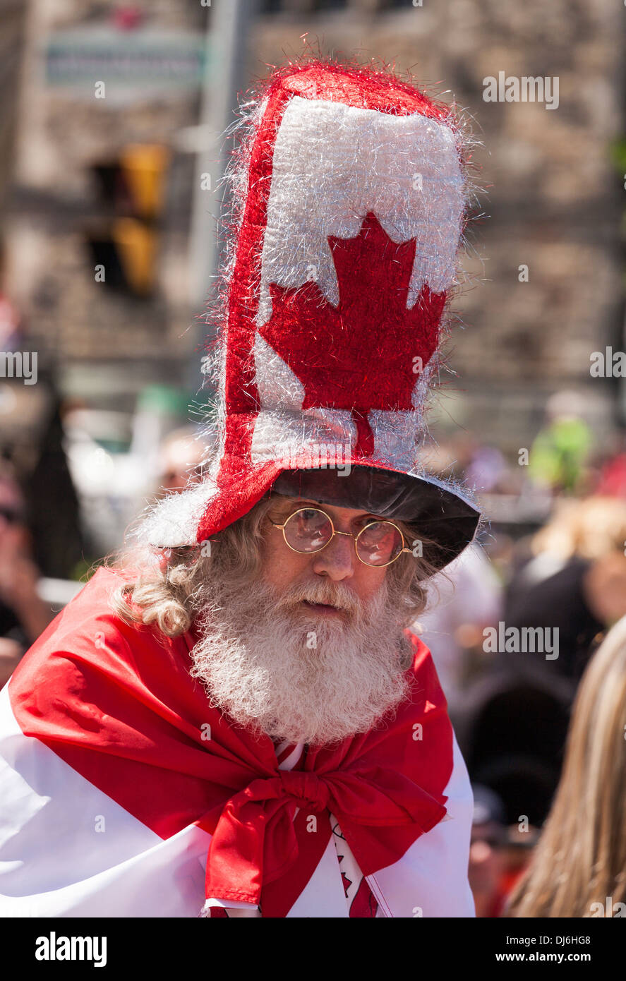 Bärtiger Mann in einem großen Ahorn Blatt Hut und eingehüllt in eine Fahne. Patriotische Zelebrant Spaziergänge durch die Menschenmassen am Canada Day Stockfoto