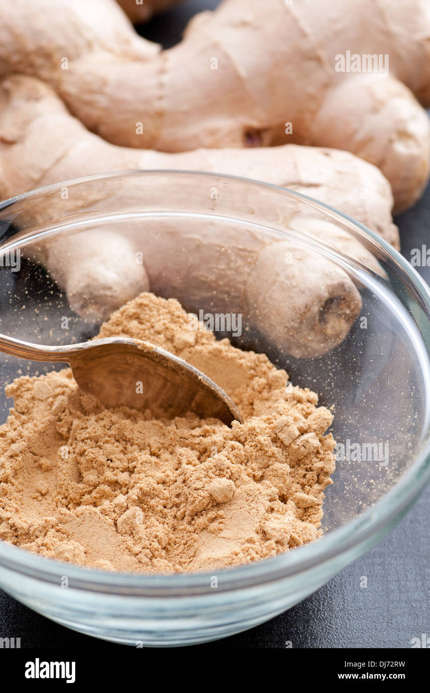 Eine Schüssel mit gemahlenem Ingwer und frischem Ingwer im Hintergrund. Stockfoto
