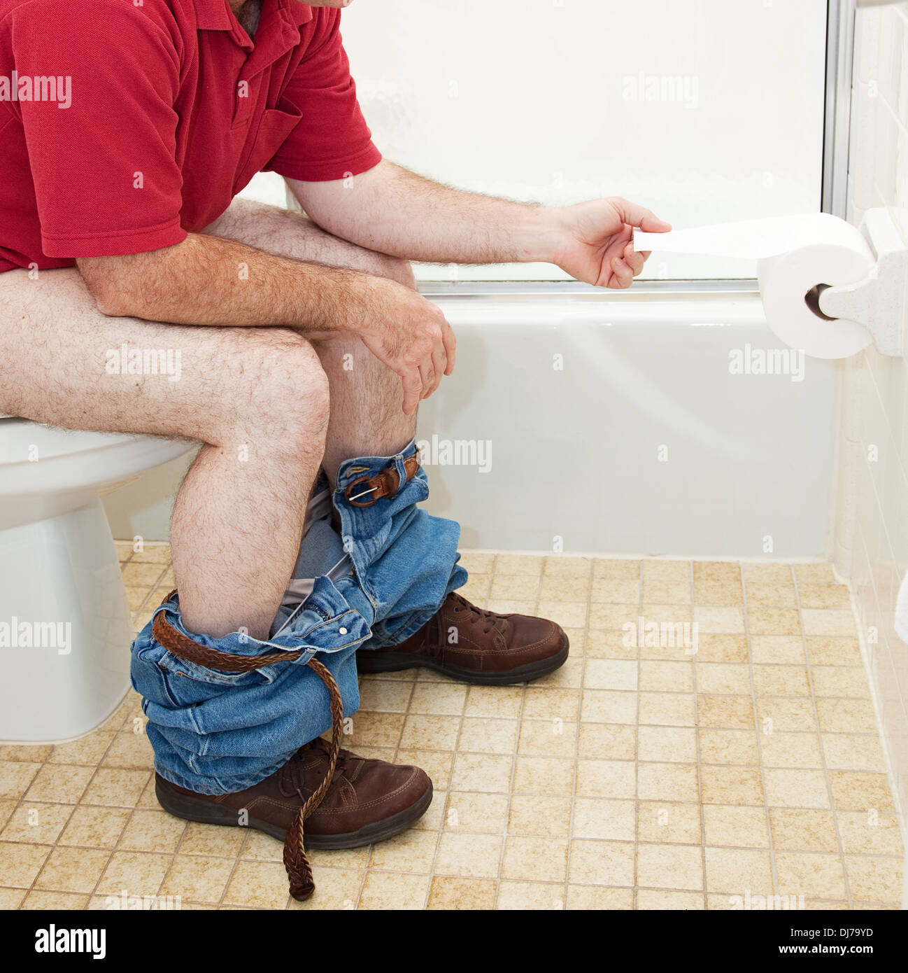 Mann im Bad auf der Toilette sitzt ein Stück Toilettenpapier abziehen. Stockfoto